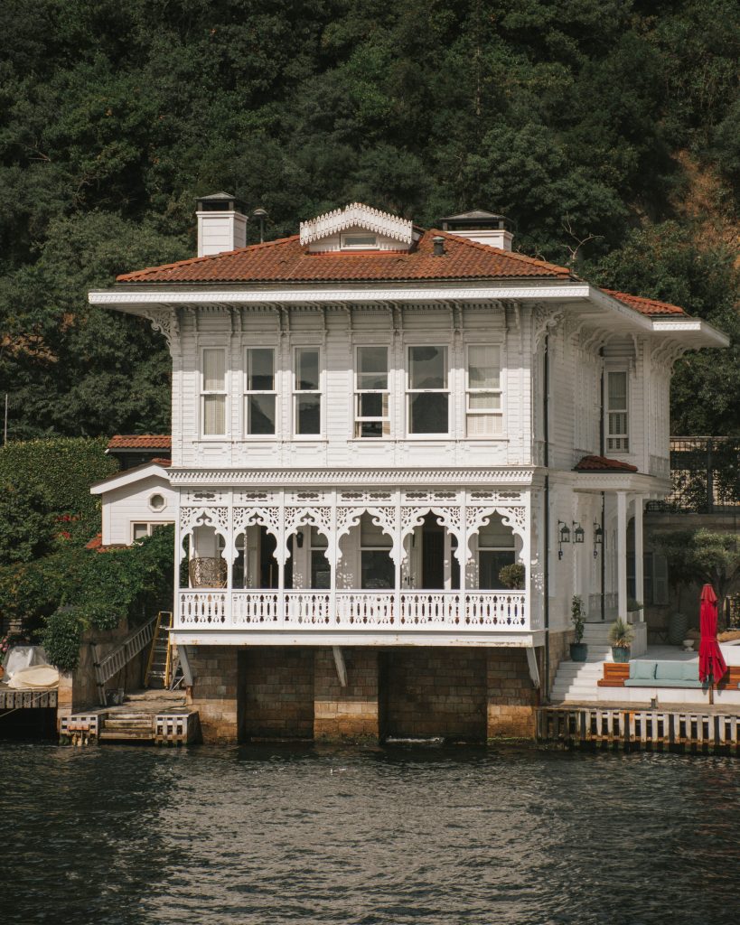 A picturesque, ornate villa by the waterfront surrounded by lush greenery and intricate architectural details.